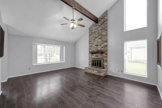 an empty room with wooden floor chandelier fan and windows