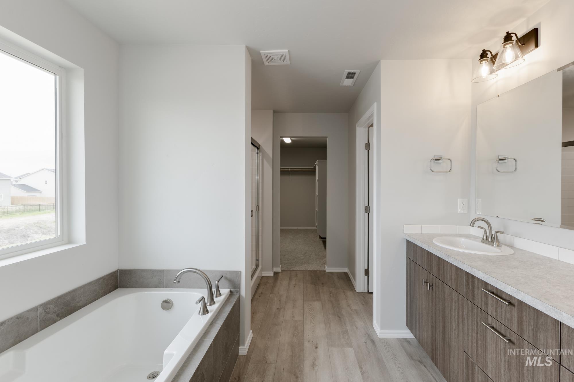12842 Ropers Street Nampa, ID 83651 - Photo 27 of 29 Bathroom featuring a built-in soaking tub with gray tile surround, single vanity with light-toned countertop, wood-finish flooring, and a large window