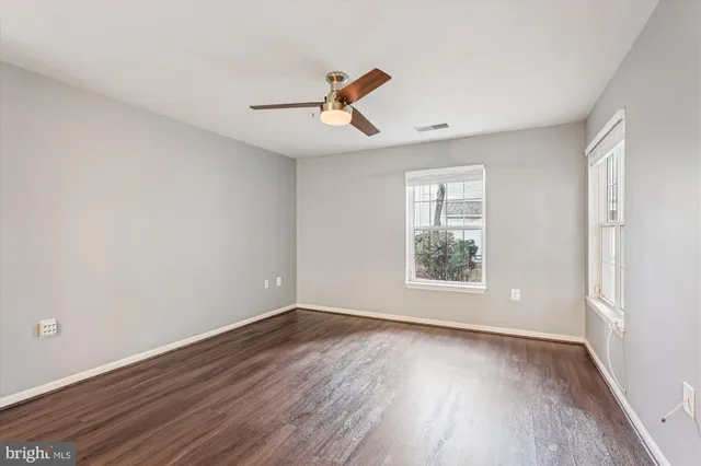 an empty room with wooden floor ceiling fan and windows