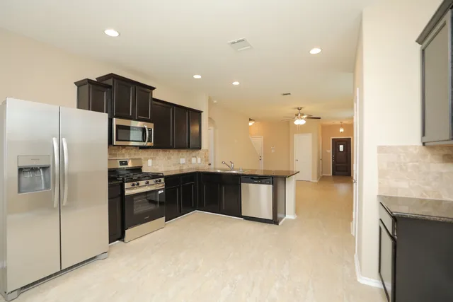 a large kitchen with stainless steel appliances kitchen island granite countertop a refrigerator a sink a stove and cabinets