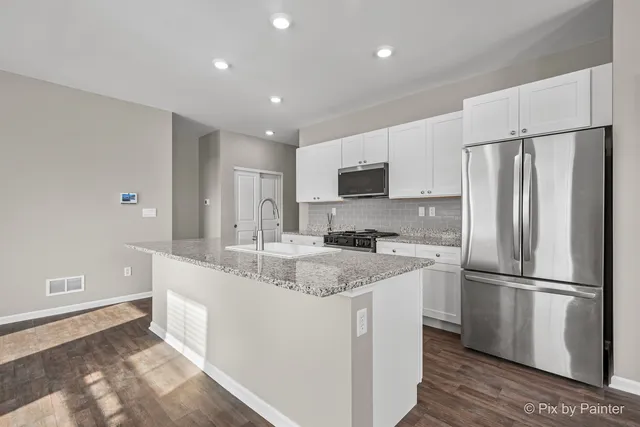 a kitchen with stainless steel appliances granite countertop a refrigerator a sink a stove a microwave and white cabinets with wooden floor