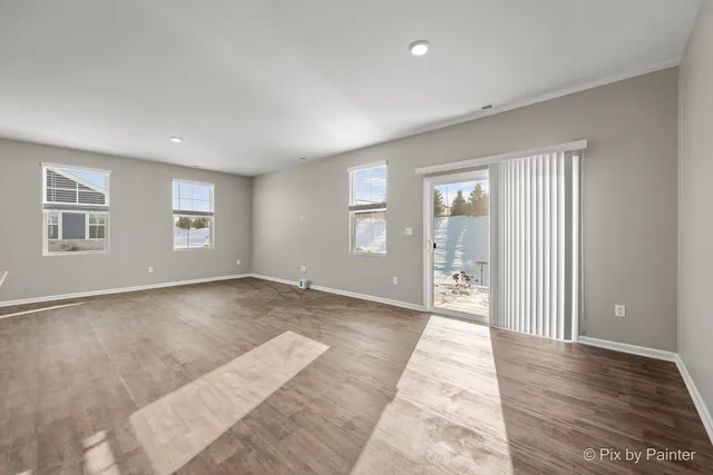 a view of an empty room with wooden floor and windows