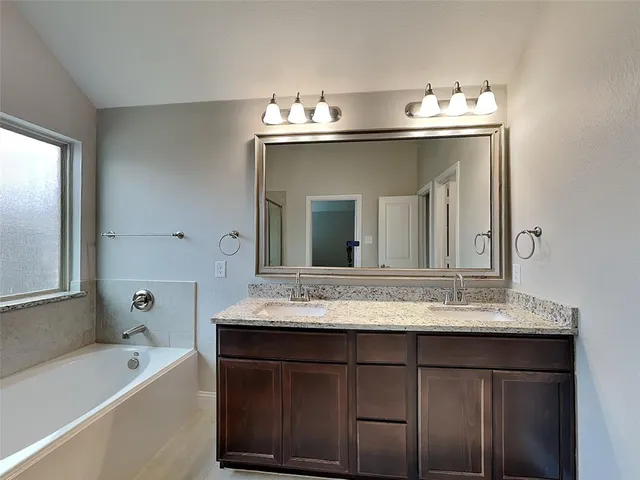 a bathroom with a sink vanity granite tub and a mirror