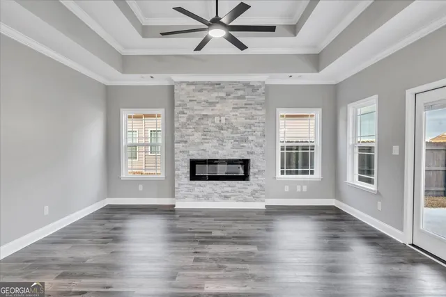 an empty room with wooden floor a fireplace a ceiling fan and windows