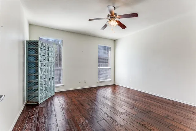 an empty room with wooden floor chandelier fan and windows