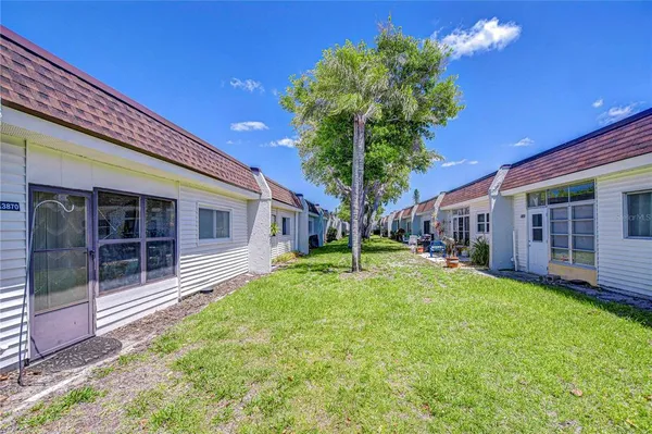 a yellow house in front of a brick house with a large tree and a yard