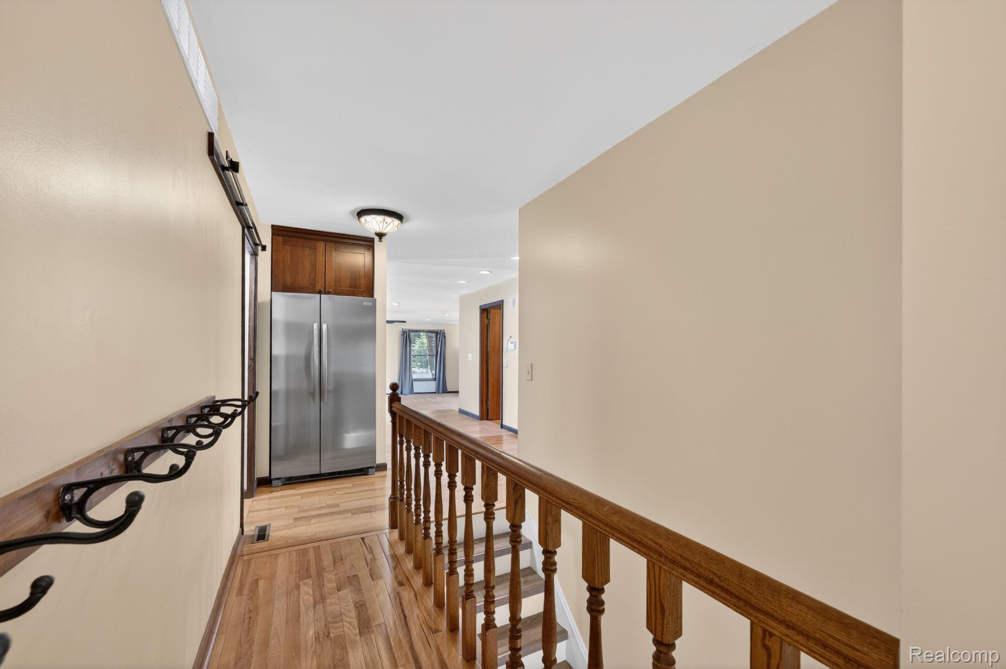 9353 Hill Road Swartz Creek, MI 48473 - Photo 26 of 98 Hallway featuring hardwood flooring, natural wood staircase with spindles, stainless steel refrigerator, dark wood cabinetry, and a black metal coat rack