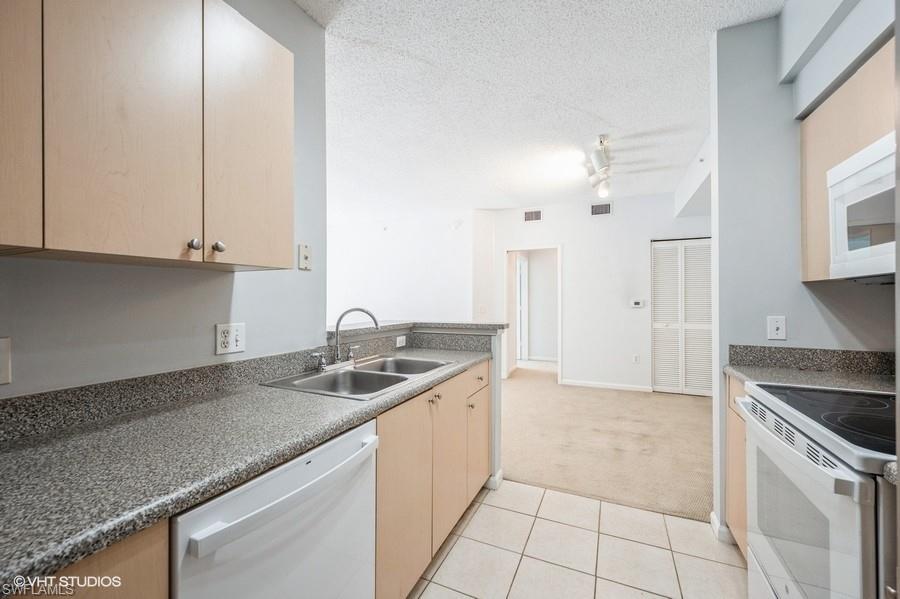 1170 Reserve Way, Unit 107 Naples, FL 34105 - Photo 11 of 41 Kitchen with sink, white appliances, light carpet, light brown cabinets, and a textured ceiling