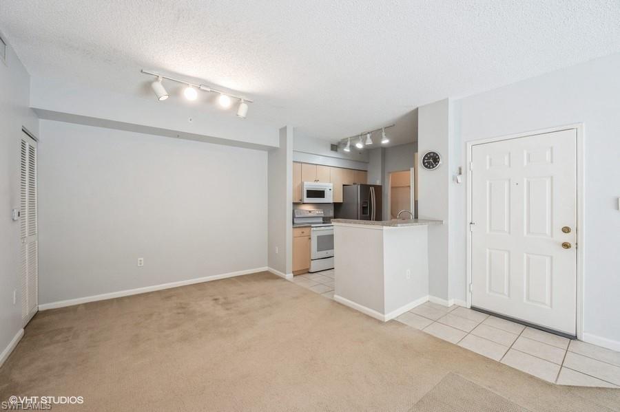 1170 Reserve Way, Unit 107 Naples, FL 34105 - Photo 12 of 41 Kitchen featuring a textured ceiling, light carpet, light brown cabinetry, and white appliances