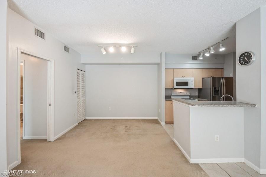 1170 Reserve Way, Unit 107 Naples, FL 34105 - Photo 13 of 41 Kitchen featuring light carpet, electric range oven, a textured ceiling, stainless steel fridge, and kitchen peninsula