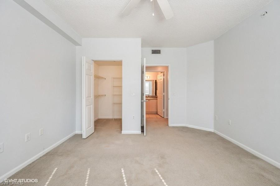 1170 Reserve Way, Unit 107 Naples, FL 34105 - Photo 21 of 41 Unfurnished bedroom with a walk in closet, light colored carpet, ceiling fan, a textured ceiling, and a closet