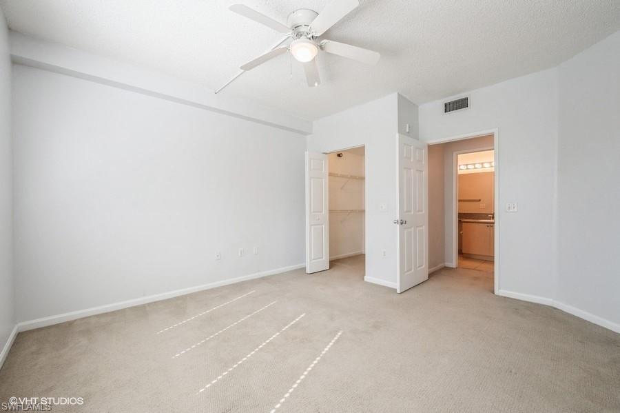 1170 Reserve Way, Unit 107 Naples, FL 34105 - Photo 22 of 41 Unfurnished bedroom featuring ceiling fan, a textured ceiling, light carpet, a spacious closet, and a closet