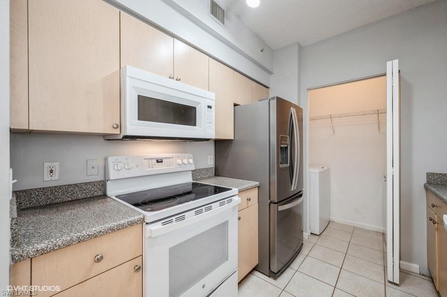 1170 Reserve Way, Unit 107 Naples, FL 34105 - Photo 9 of 41 Kitchen with light tile patterned floors, white appliances, light brown cabinets, a textured ceiling, and washer and clothes dryer