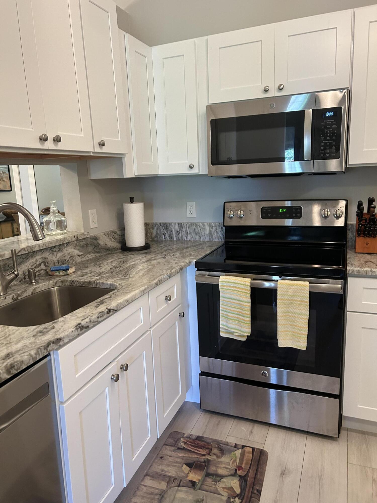 6504 Chasewood Drive, Unit H Jupiter, FL 33458 - Photo 2 of 8 a kitchen with granite countertop white cabinets and stainless steel appliances