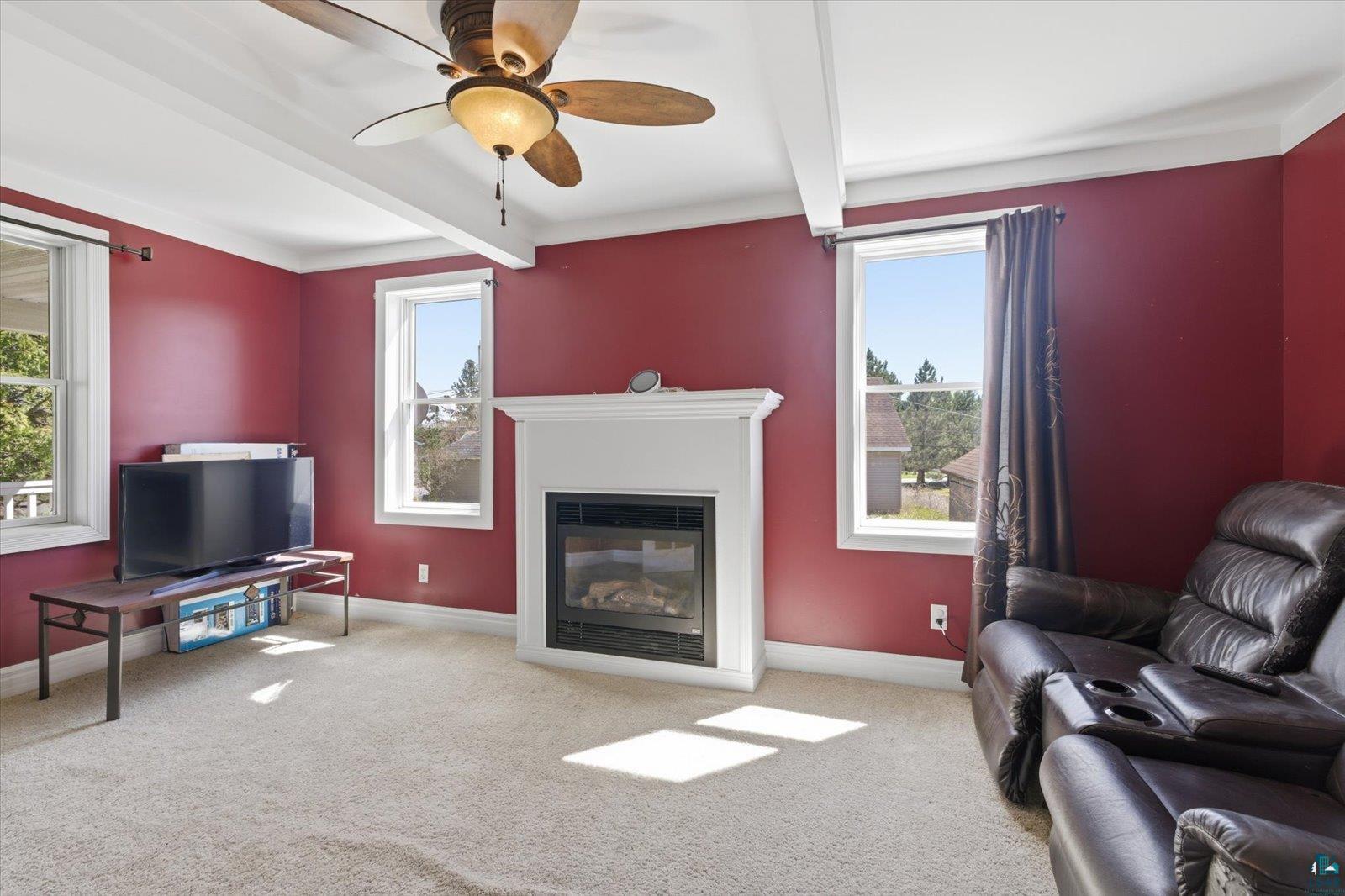 50 Main Street Soudan, MN 55782 - Photo 7 of 31 Living space with a white mantel fireplace, two large windows, exposed ceiling beams, and a ceiling fan