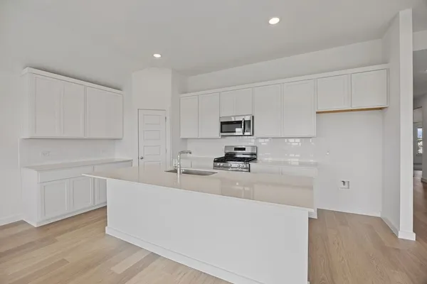 a kitchen with stainless steel appliances a sink a stove a refrigerator and white cabinets