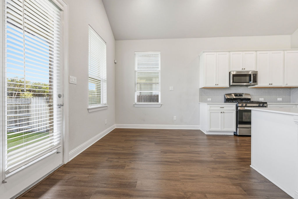 2032 Base Burner Path Leander, TX 78641 - Photo 15 of 34 Open-concept living area featuring wood-finish flooring, vaulted ceilings, and a kitchen with white cabinetry, stainless steel appliances, and a tiled backsplash