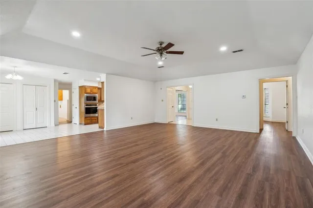 an empty room with wooden floor ceiling fan and windows