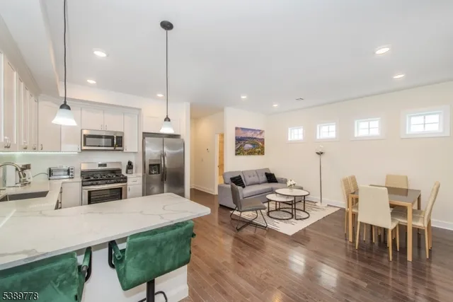 a kitchen with stainless steel appliances kitchen island granite countertop a dining table chairs and a refrigerator