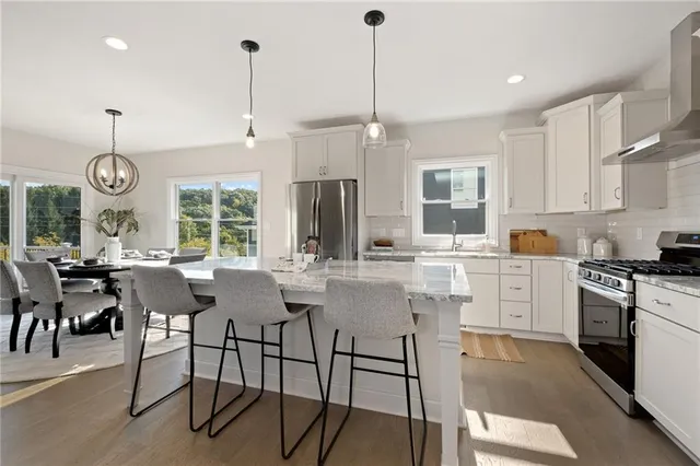 a kitchen with stainless steel appliances granite countertop a stove a refrigerator a kitchen island a dining table and chairs with wooden floor