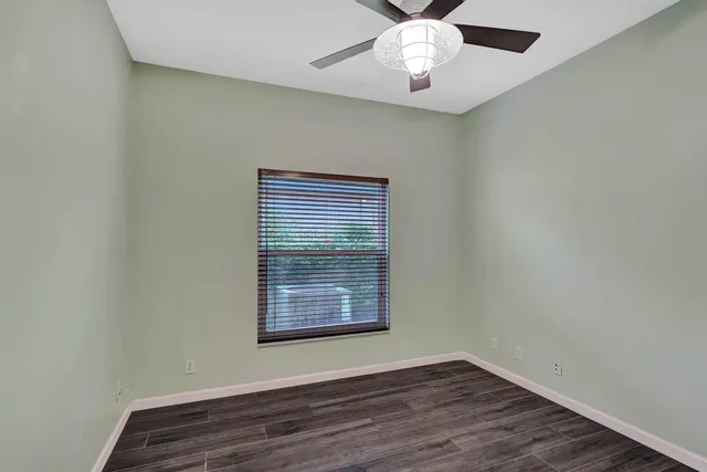 an empty room with wooden floor fan and windows