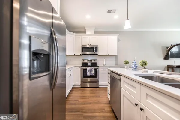 a kitchen with stainless steel appliances granite countertop a refrigerator a stove a sink and white cabinets with wooden floor