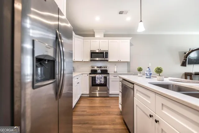 a kitchen with stainless steel appliances granite countertop a refrigerator a stove a sink and white cabinets with wooden floor