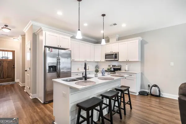 a kitchen with stainless steel appliances kitchen island granite countertop a refrigerator a stove a sink dishwasher and white cabinets with wooden floor