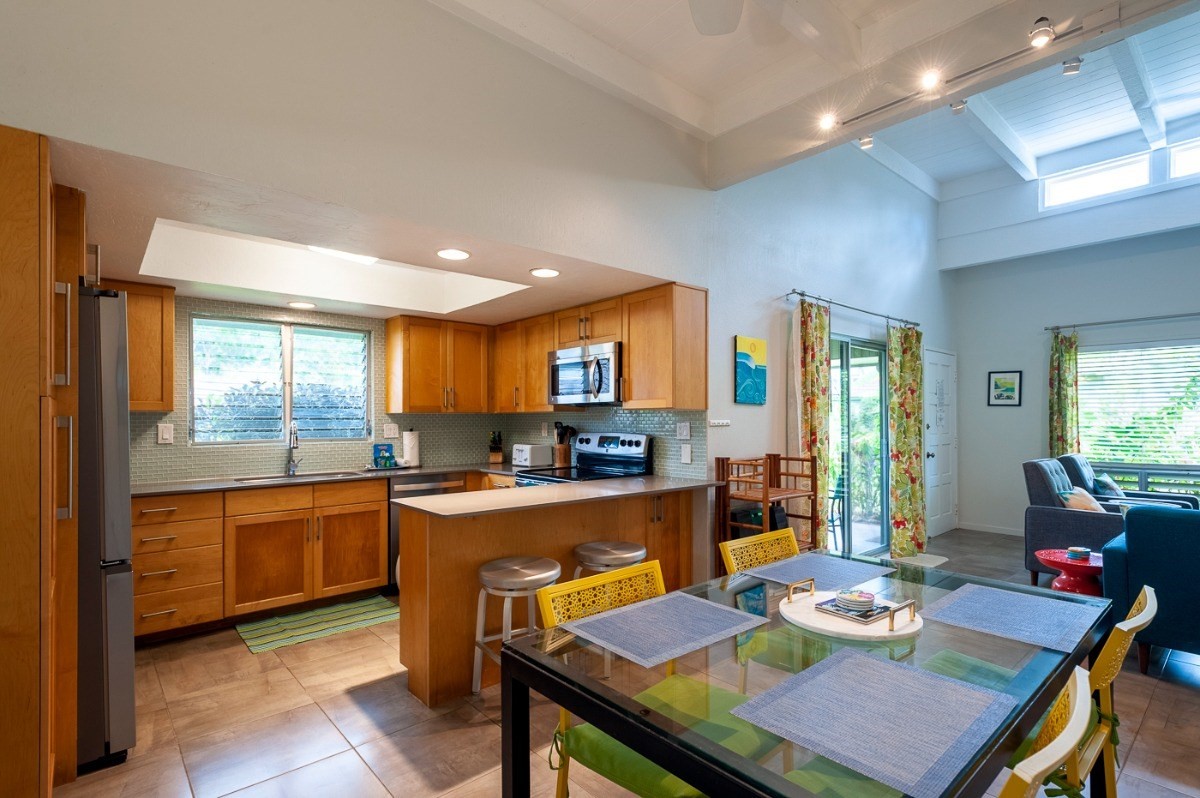 3880 Wyllie Road, Unit 1A Princeville, HI 96722 - Photo 8 of 22 a kitchen with a stove a sink dishwasher and a dining table with garden view