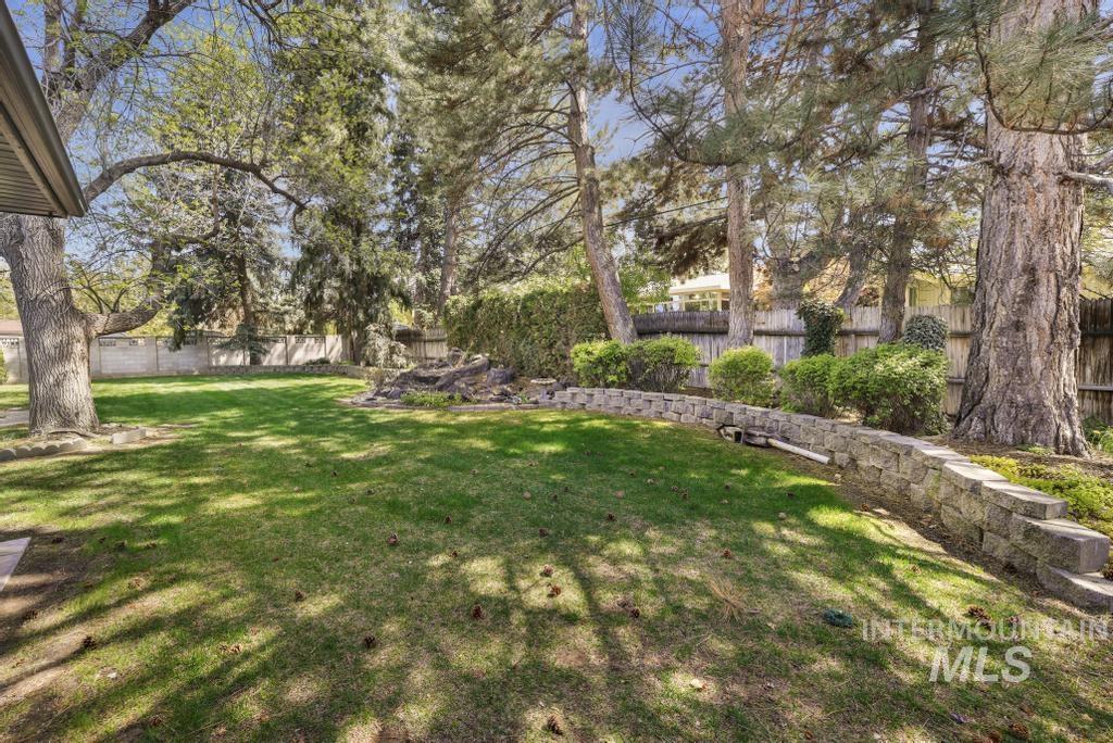 2018 Rancho Vista Drive Twin Falls, ID 83301 - Photo 45 of 50 Expansive backyard featuring a lush lawn, mature trees providing natural shade, a stone-block retaining wall, established shrubbery, and a wood privacy fence