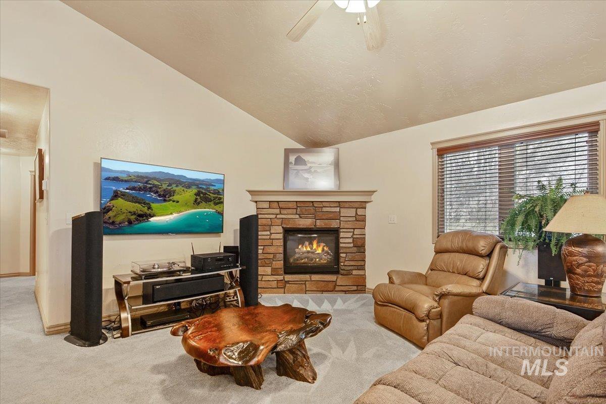 1513 Fairway Street Middleton, ID 83644 - Photo 4 of 20 Carpeted living area featuring vaulted ceiling, a stone fireplace, ceiling fan, and a textured ceiling