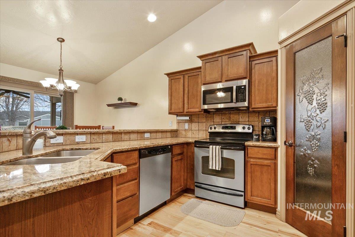 1513 Fairway Street Middleton, ID 83644 - Photo 5 of 20 Kitchen with appliances with stainless steel finishes, brown cabinetry, light stone counters, pendant lighting, and lofted ceiling