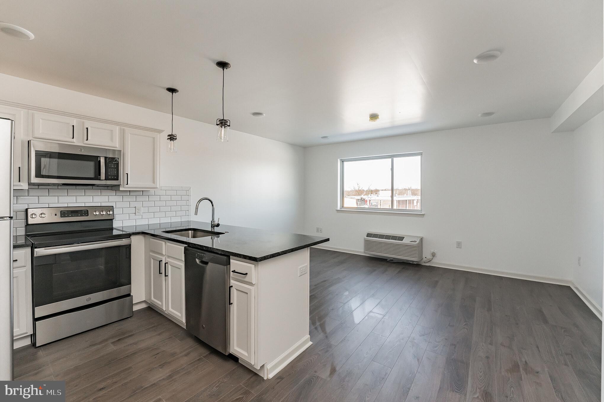 6649 Ridge Avenue, Unit A407 Philadelphia, PA 19128 - Photo 1 of 7 a kitchen with granite countertop a stove and a wooden floor
