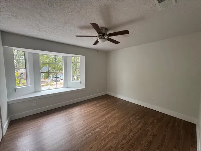 an empty room with wooden floor fan and windows