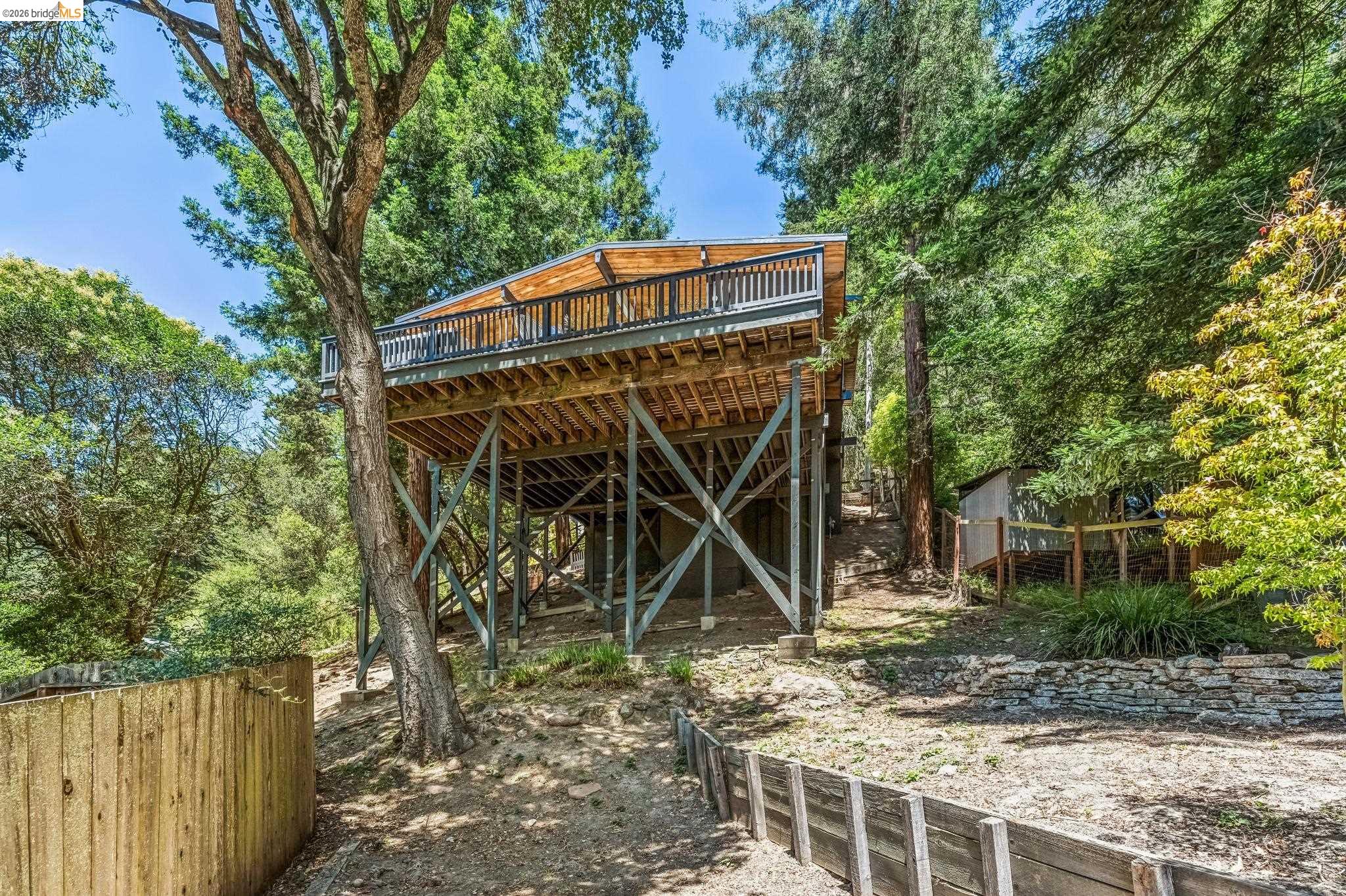 6645 Heather Ridge Way Oakland, CA 94611 - Photo 58 of 61 Elevated property structure featuring a wood plank deck with a dark metal railing, set amidst mature trees