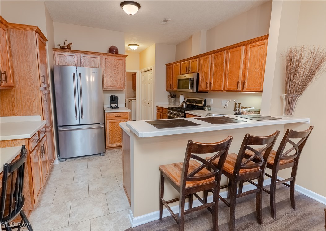 5645 Clingan Road, Unit 23B Struthers, OH 44471 - Photo 4 of 38 Kitchen featuring a kitchen breakfast bar, appliances with stainless steel finishes, a peninsula, brown cabinets, and light tile patterned floors