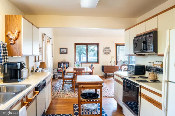 a open kitchen with stainless steel appliances granite countertop a stove top oven a sink dishwasher a dining table and chairs with wooden floor