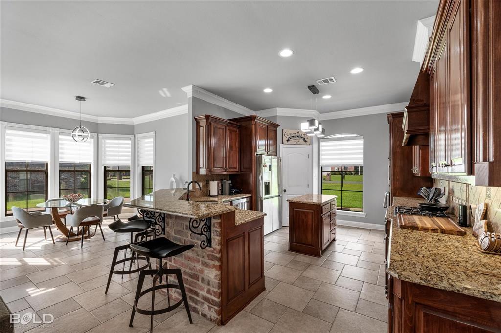 2220 Forest Hills Boulevard Haughton, LA 71037 - Photo 13 of 40 Kitchen featuring wood cabinetry, granite countertops, tile flooring, a brick-front breakfast bar with decorative corbels, and a bay window dining area with contemporary lighting