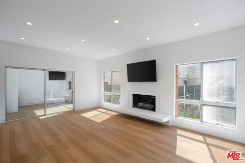 a view of an empty room with wooden floor a fireplace and a window