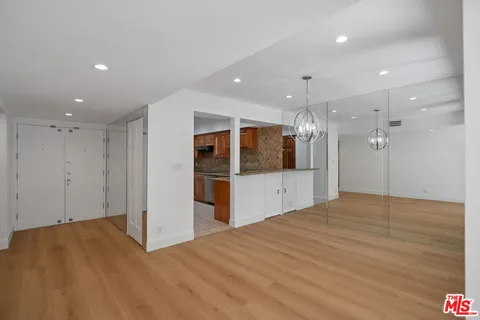 a view of an empty room with kitchen and window
