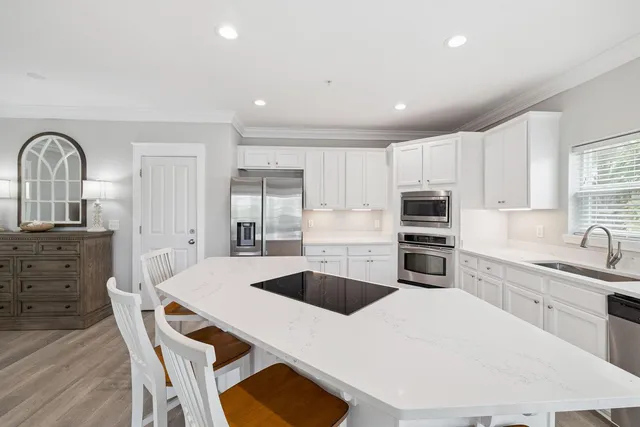 a kitchen with stainless steel appliances a sink a stove a refrigerator cabinets a dining table and chairs