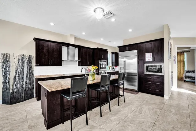 a kitchen with stainless steel appliances kitchen island granite countertop a refrigerator a stove a microwave oven a dining table and chairs with wooden floor