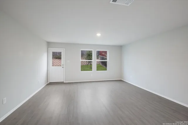 a view of an empty room with wooden floor and window