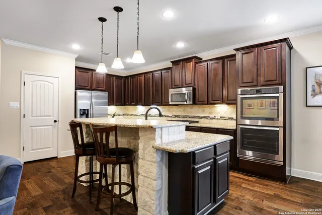 a kitchen with kitchen island granite countertop wooden cabinets a refrigerator a stove a sink and a center island