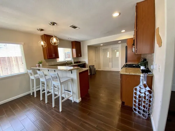 a kitchen with stainless steel appliances kitchen island granite countertop a stove a sink a refrigerator and a dining table with wooden floor