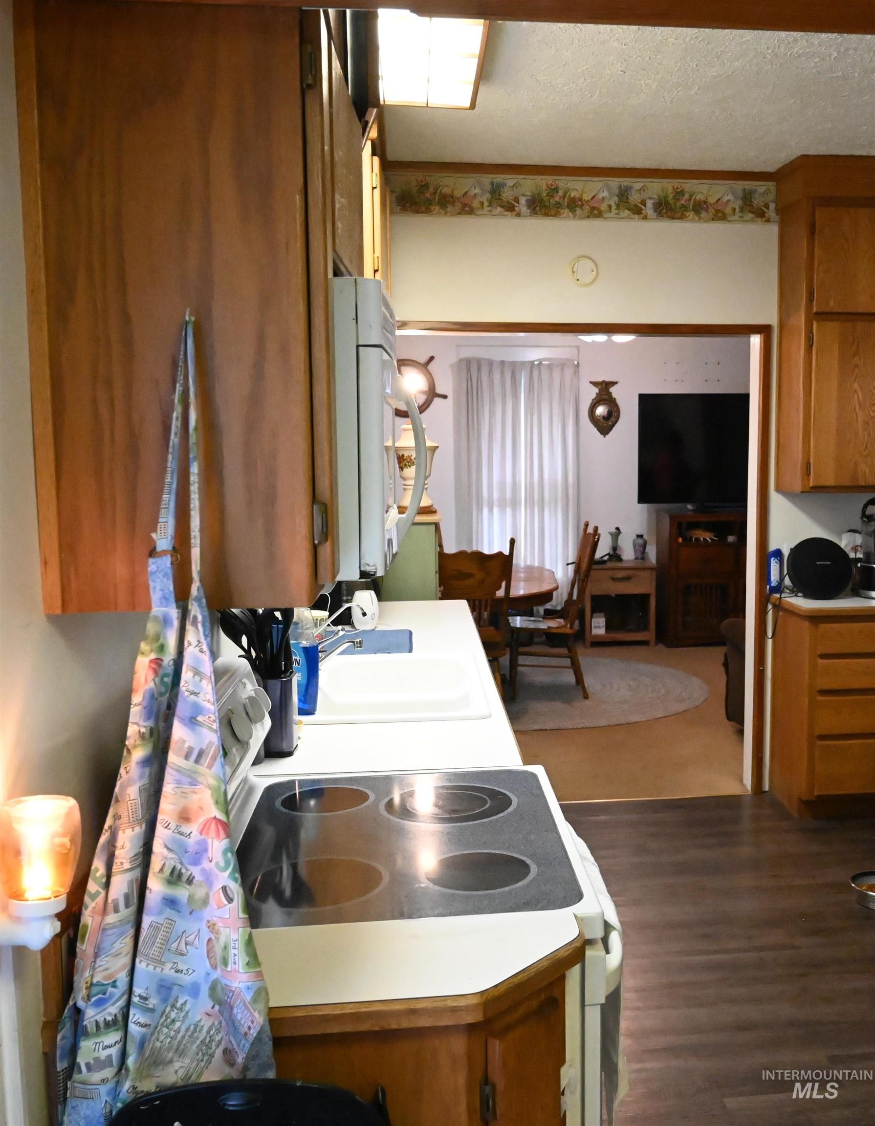 646 Riverside Avenue Orofino, ID 83544 - Photo 13 of 23 Kitchen featuring brown cabinetry, white appliances, light countertops, dark wood-style floors, and a textured ceiling
