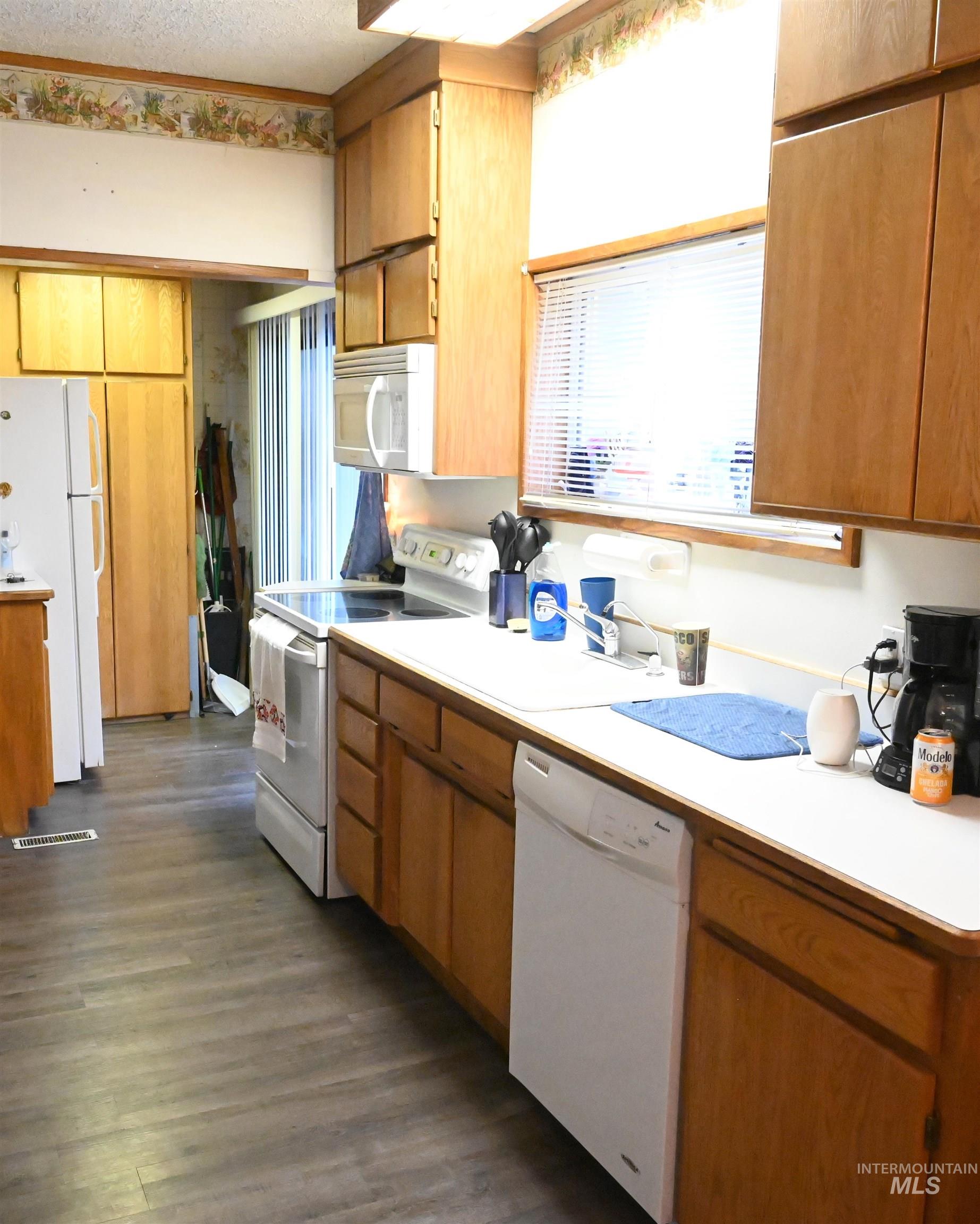 646 Riverside Avenue Orofino, ID 83544 - Photo 5 of 23 Kitchen featuring light countertops, white appliances, brown cabinets, a textured ceiling, and dark wood-style floors