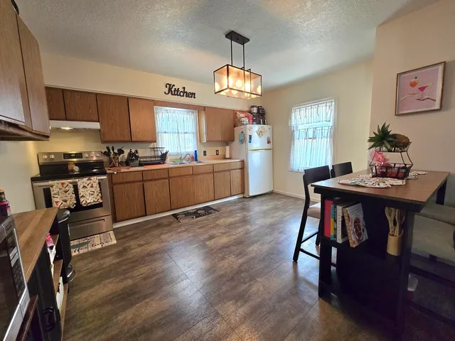 a kitchen with stainless steel appliances granite countertop a stove top oven a refrigerator a sink dishwasher a dining table and chairs with wooden floor