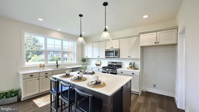 a kitchen with stainless steel appliances kitchen island a sink a stove a refrigerator and white cabinets with wooden floor