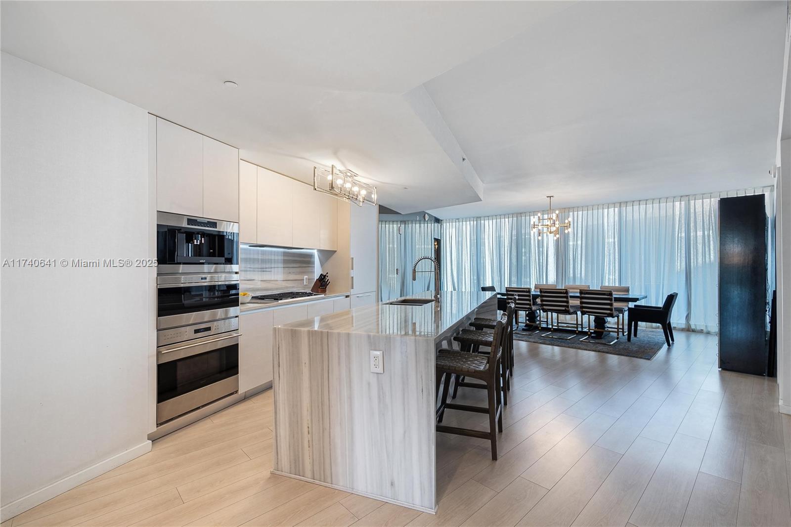 1 Collins Avenue, Unit 304 Miami Beach, FL 33139 - Photo 13 of 40 a kitchen with stainless steel appliances granite countertop a stove top oven a refrigerator a dining table and chairs with wooden floor